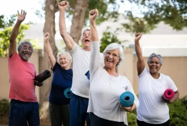 Group of active older adults smiling and raising their arms in celebration outdoors while holding yoga mats, representing community wellness and lifestyle programming. The adjacent text promotes lifestyle management services at Empire Management Group.